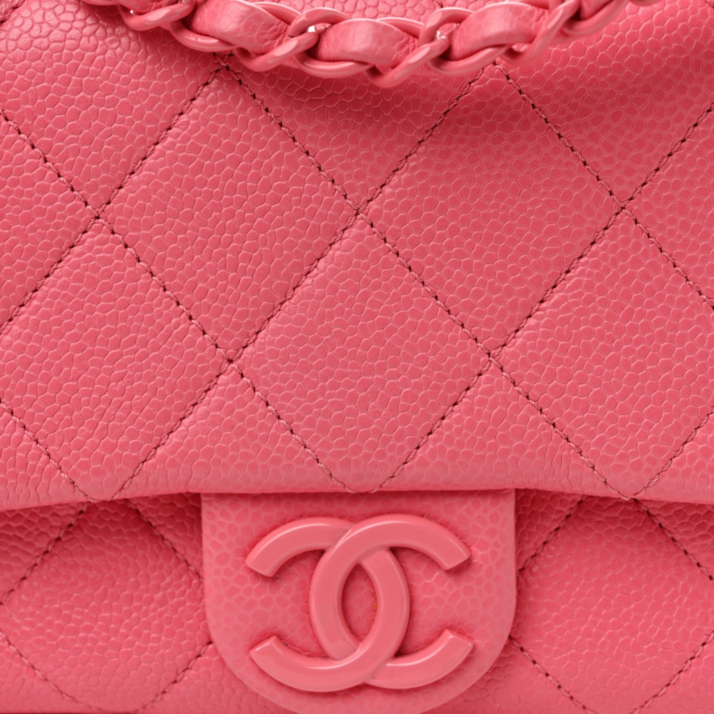 A detailed close-up of a pink quilted leather classic flap bag, focusing on the pink enamel interlocking CC clasp and the pink leather-interwoven chain strap, illustrating a classic design.